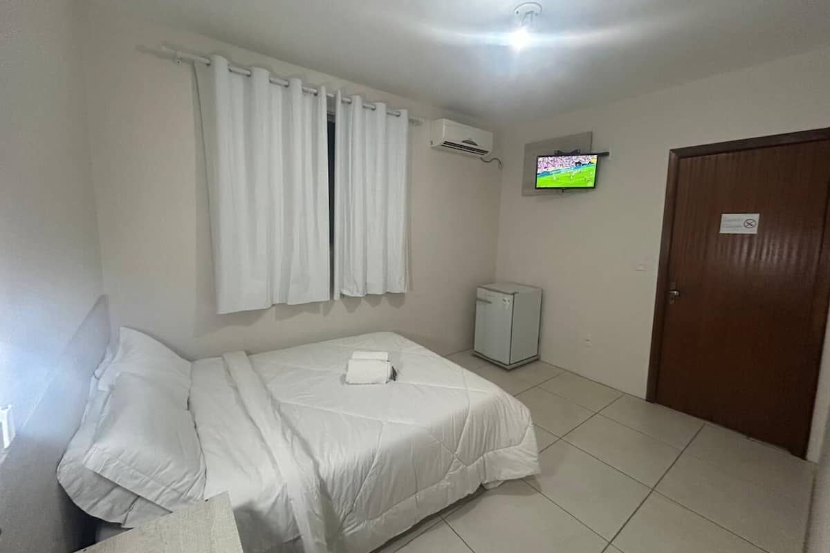 Une chambre d’hôtel équipée d’un lit, d’une télévision, d’un climatiseur, d’un petit réfrigérateur et d’une porte.