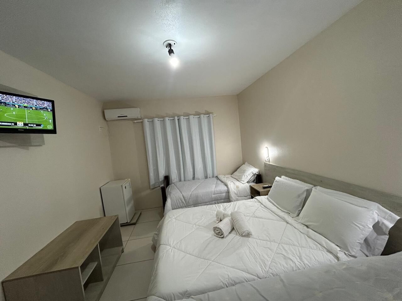 Une chambre d’hôtel avec deux lits, une télévision, un bureau et une fenêtre avec des rideaux.
