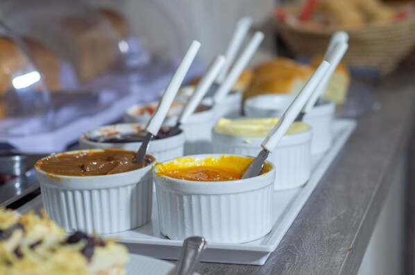 Una barra de buffet con diversos platos en recipientes blancos, incluyendo un postre de chocolate y una crema pastelera amarilla.