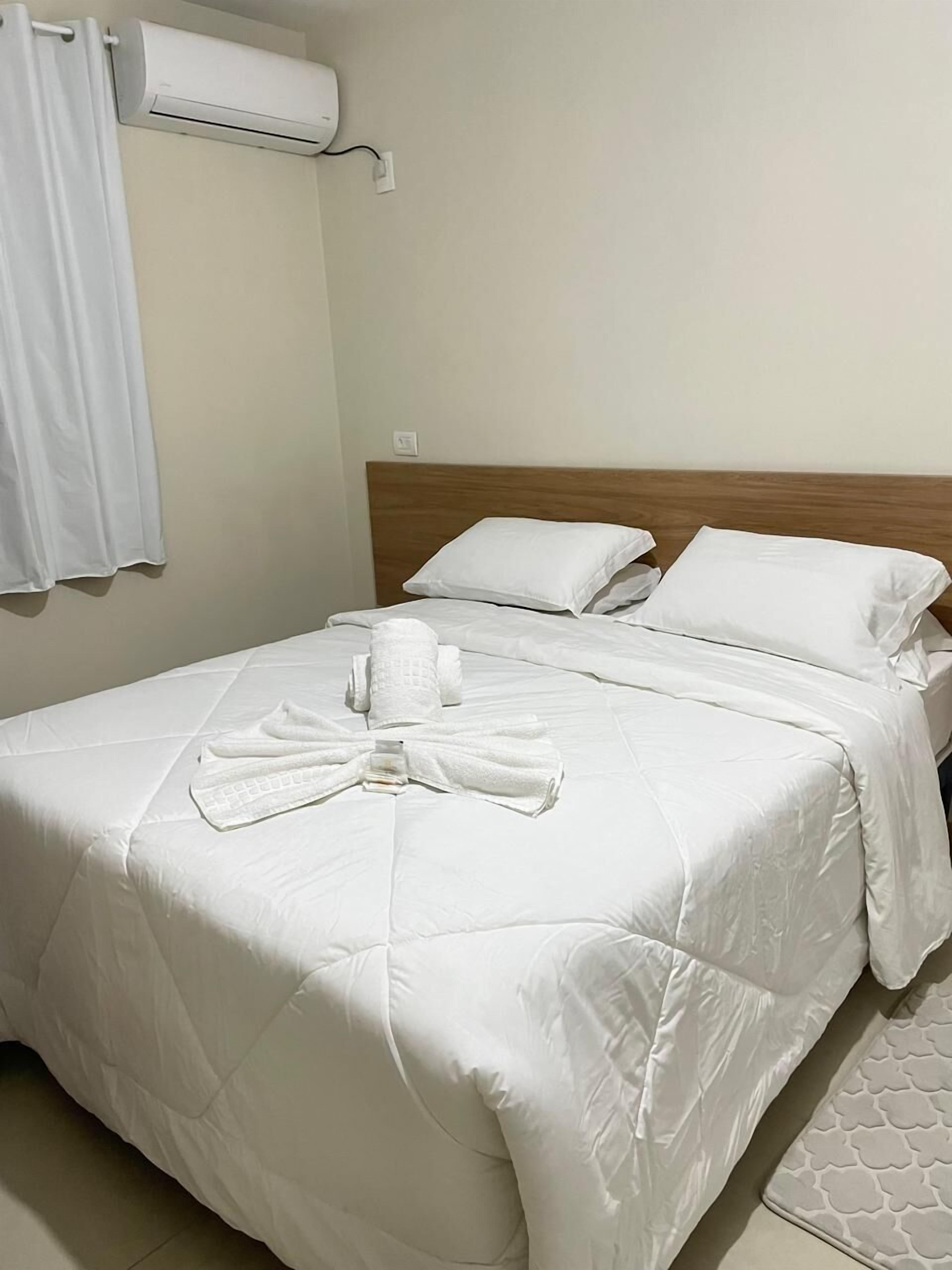 Una cama bien hecha con sábanas blancas y una toalla doblada en forma de lazo.