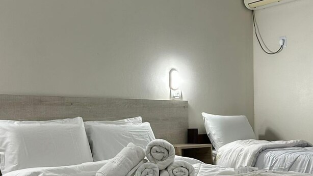 Habitación de hotel con cama, mesita de noche, aire acondicionado de pared y luz de pared.