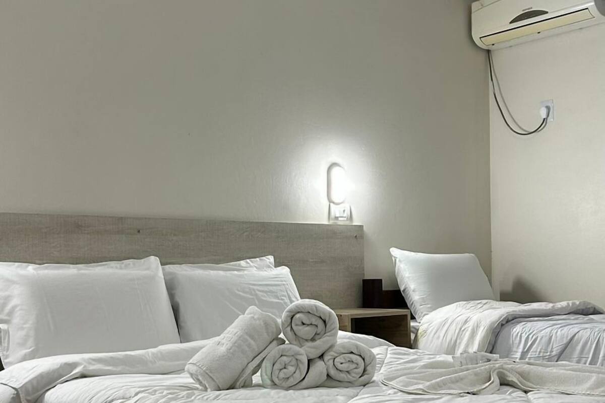 Une chambre d’hôtel comprenant un lit, une table de chevet, un climatiseur fixé au mur et une lampe fixée au mur.