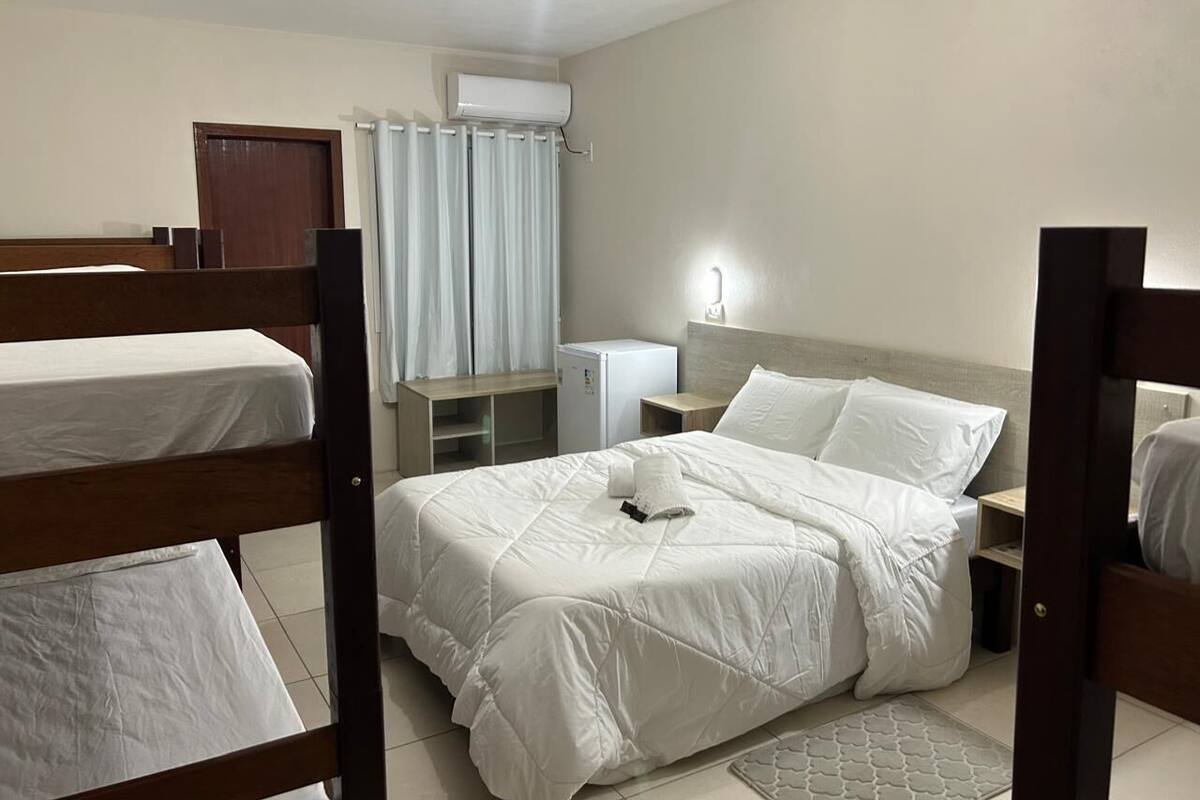 Une chambre d’hôtel avec des lits superposés, un bureau, une chaise, un petit réfrigérateur et une table de chevet avec une lampe.