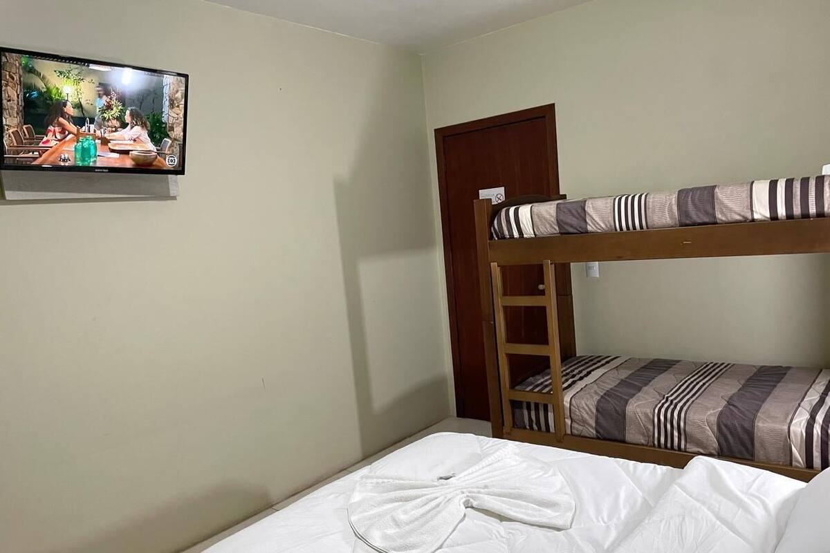 Une pièce avec un lit superposé, un lit simple recouvert d’une couverture blanche, un tableau accroché au mur et une porte.