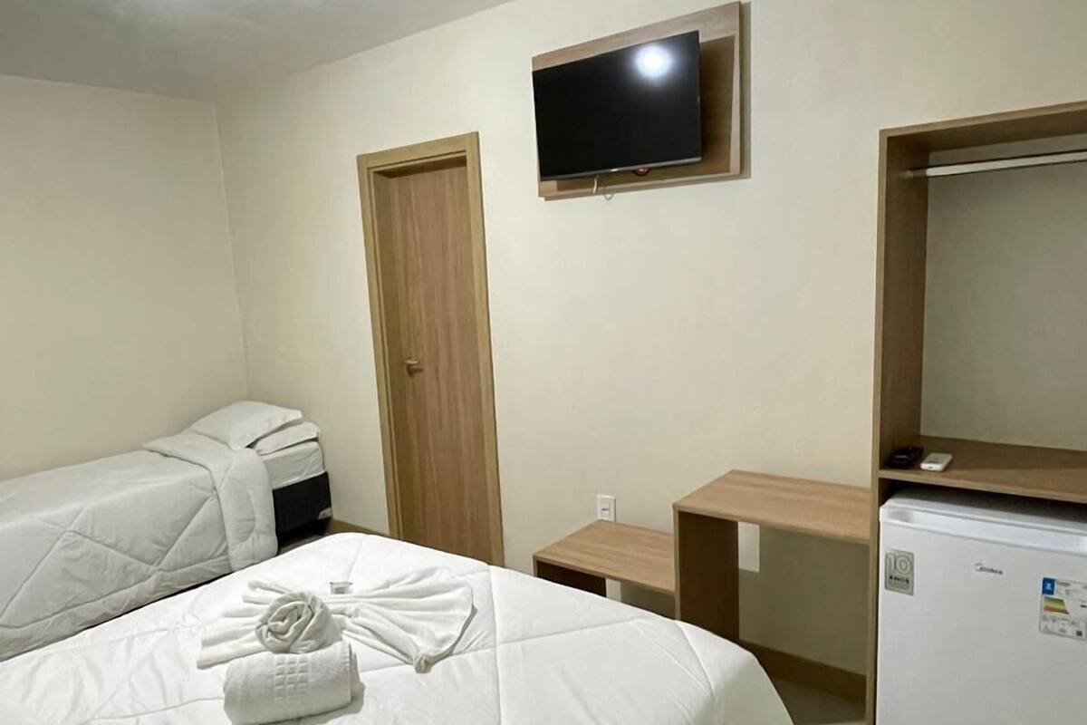 Une chambre d’hôtel avec deux lits, une télévision, un réfrigérateur et une porte.