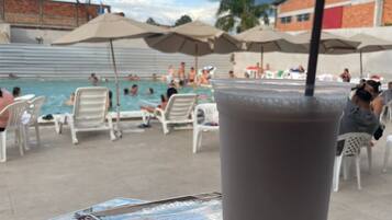 Une boisson servie dans un verre avec une paille, un menu et un espace piscine avec des personnes et des parasols.