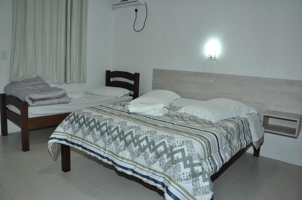 A bedroom with a bed, a bedside table, a wall-mounted air conditioner, and a window with curtains.