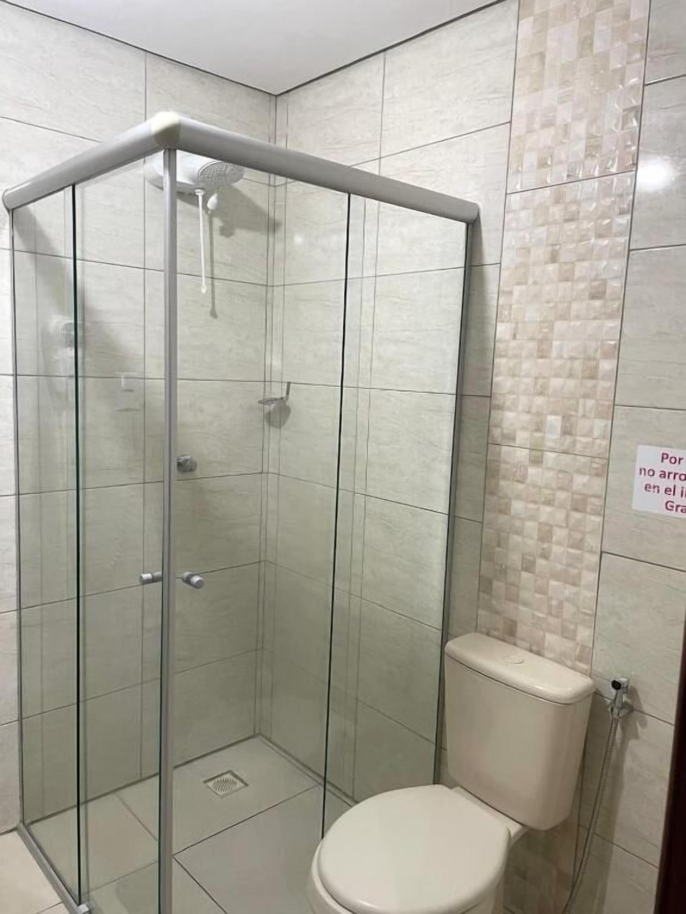 Cabina de ducha con paredes de vidrio y un inodoro contiguo.