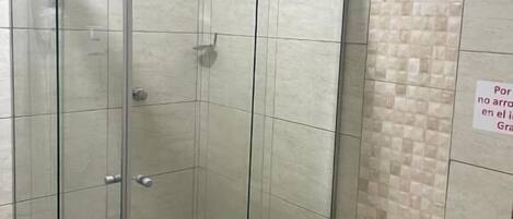 Cabina de ducha con paredes de vidrio y un inodoro contiguo.