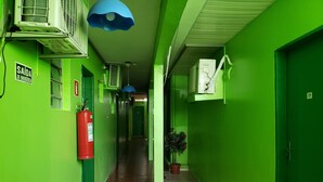 A green hallway with a fire extinguisher, emergency exit sign, and a potted plant. - Pousada Catamarã Praia de Pajuçara (Maceió)