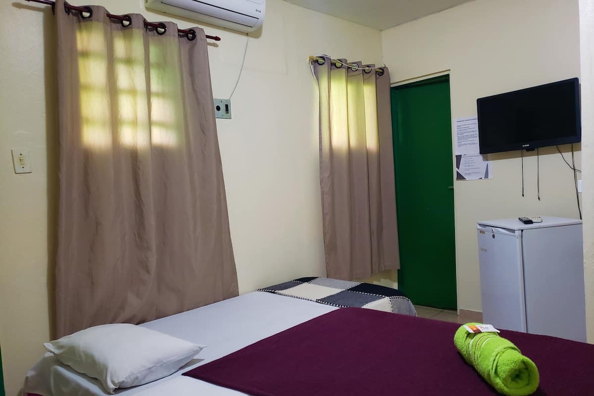Ein Hotelzimmer mit Bett, Schreibtisch mit Computer, grüner Tür und Wandklimaanlage.