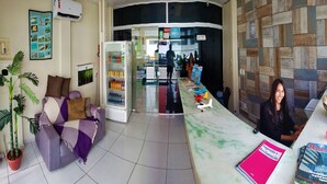 A hotel reception area with a sofa, a refrigerator stocked with beverages, a reception desk, and a wall with a bulletin board. - Pousada Catamarã Praia de Pajuçara (Maceió)