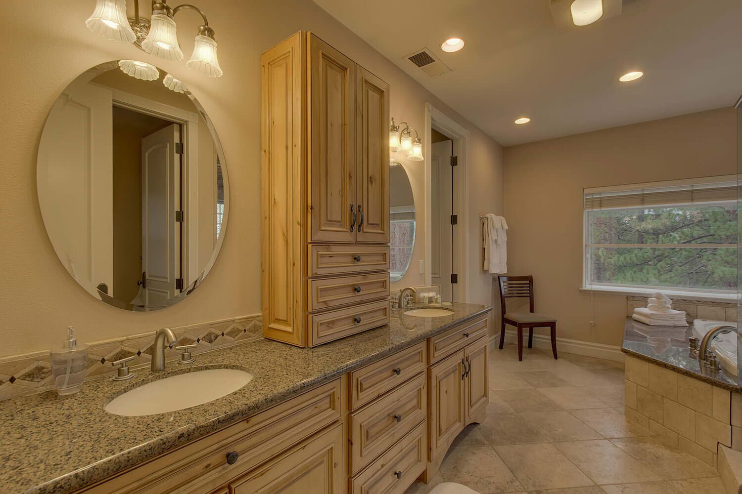 Un baño con tocador doble, muebles de madera, un espejo grande y una ventana con vista a árboles.