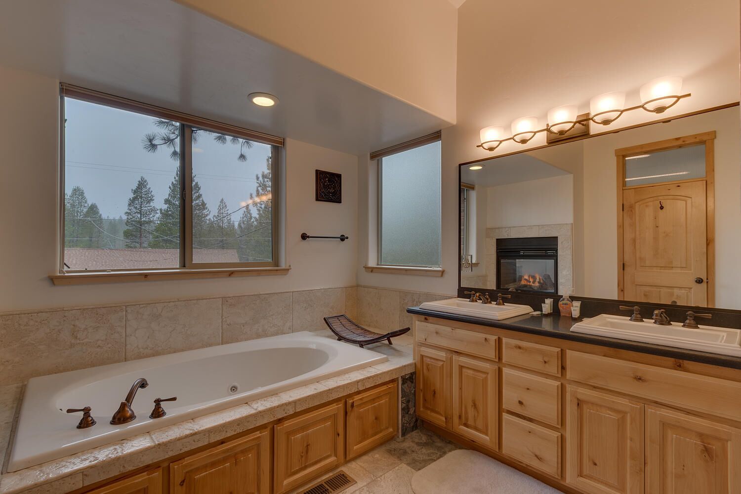 A modern bathroom with a freestanding bathtub, double vanity with a large mirror, and a fireplace in the background.