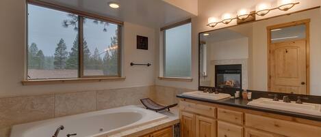 A modern bathroom with a freestanding bathtub, double vanity with a large mirror, and a fireplace in the background.