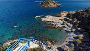 Une zone côtière caractérisée par des eaux bleues et limpides, un terrain rocheux et une plage agrémentée de parasols et de cabanes à toit de chaume.