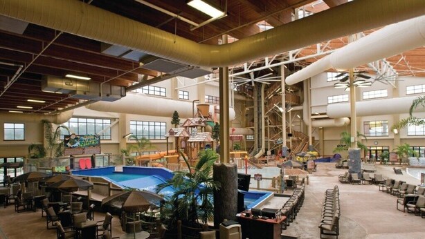 Un vaste espace intérieur comprenant une grande piscine, plusieurs coins salon et un toboggan aquatique.