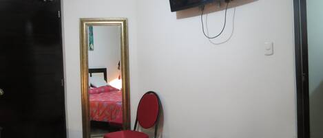 Un dormitorio con cama, una silla, un televisor y un espejo.