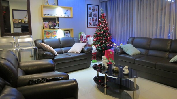A modern living room with two black leather sofas, a glass coffee table, and a Christmas tree.