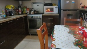 A kitchen with a stove, microwave, and refrigerator. There is a table with a festive tablecloth and two chairs.
