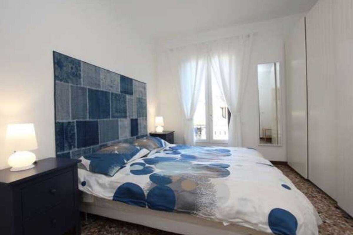 A bedroom with a bed, a nightstand, a large abstract artwork on the wall, and a window with curtains.