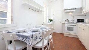 A compact kitchen with white cabinets, a microwave, and a stove. There is a dining table with chairs and a window above it. - Al Teatro Italia (Venice)