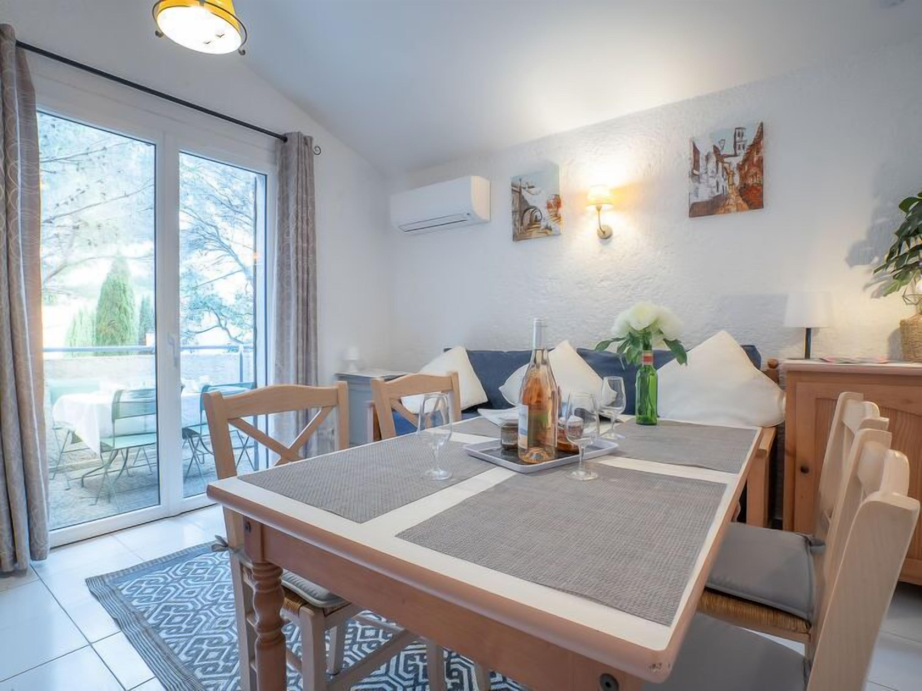 Un coin repas avec une table dressée pour deux personnes, un canapé et une vue sur un balcon.