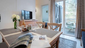 A dining area with a table set for two, a television on a stand, and a view of the outdoors through a sliding glass door. - Résidence Les Jardins d'Azur by Interhome (Saint-Raphaël)