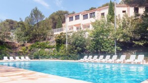 A swimming pool with white lounge chairs and a building in the background. - Résidence Les Jardins d'Azur by Interhome (Saint-Raphaël)