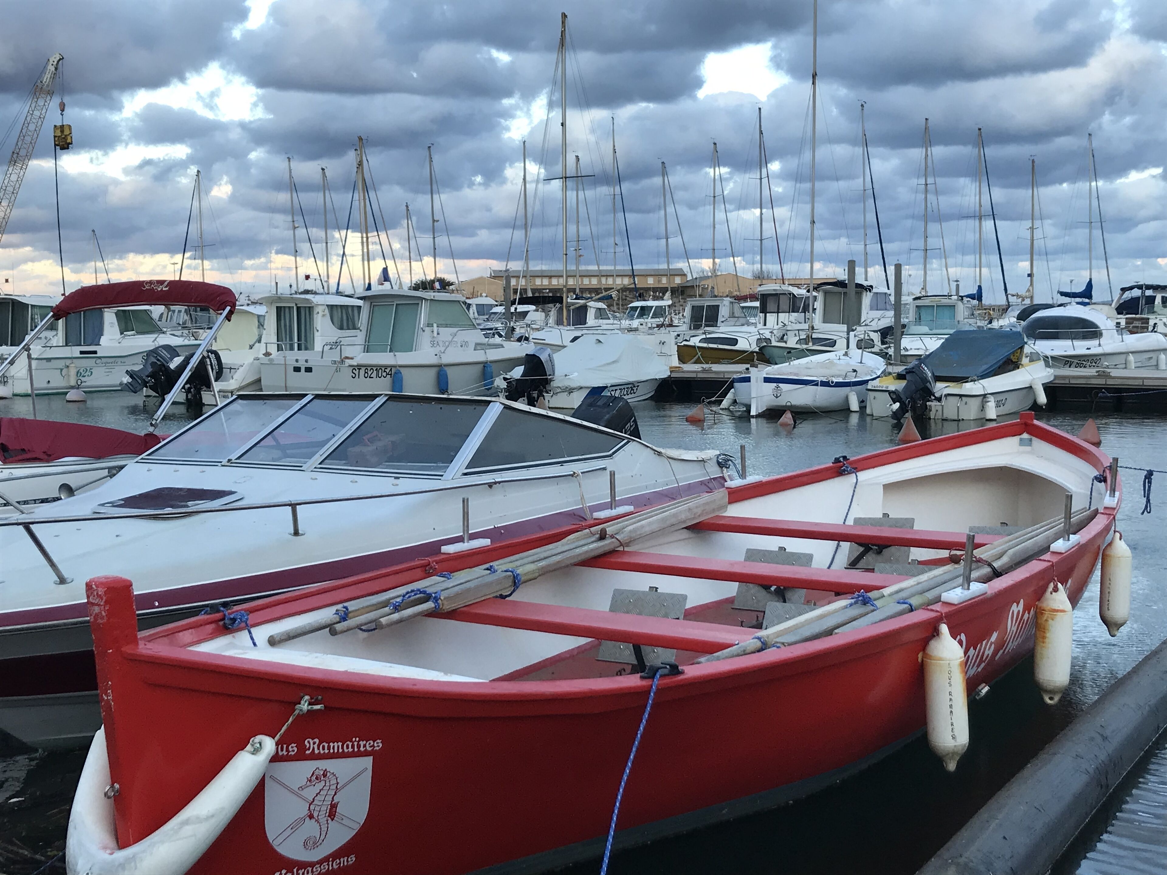 Un port de plaisance où sont amarrés plusieurs bateaux, dont un bateau rouge orné d’un logo et un bateau blanc doté d’une cabine.
