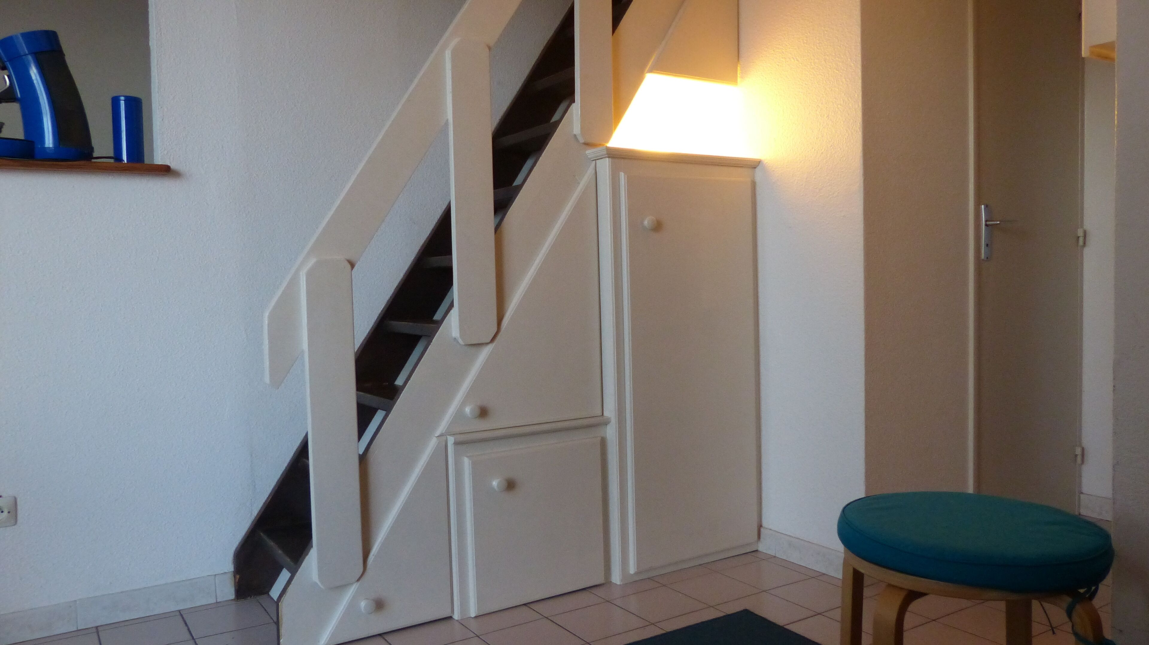 A staircase with a handrail, a door with a light switch, and a small stool.