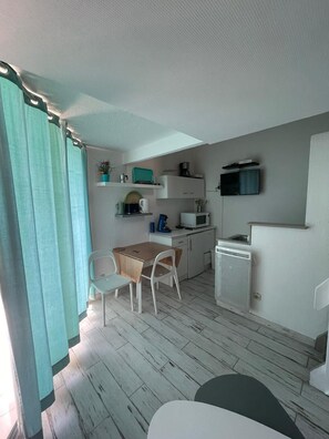 A compact kitchenette with a microwave, coffee maker, and a small refrigerator. There is a dining area with a wooden table and two chairs. A television is mounted on the wall above the kitchenette.