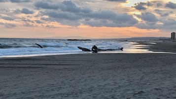 Une plage avec des vagues, un coucher de soleil et un bâtiment situé au loin.