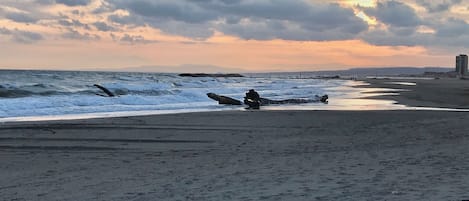 Una playa con olas, un atardecer y un edificio lejano.