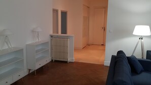 Una sala de estar moderna con un mueble blanco para entretenimiento, un radiador, un sofá azul y una lámpara de pie.