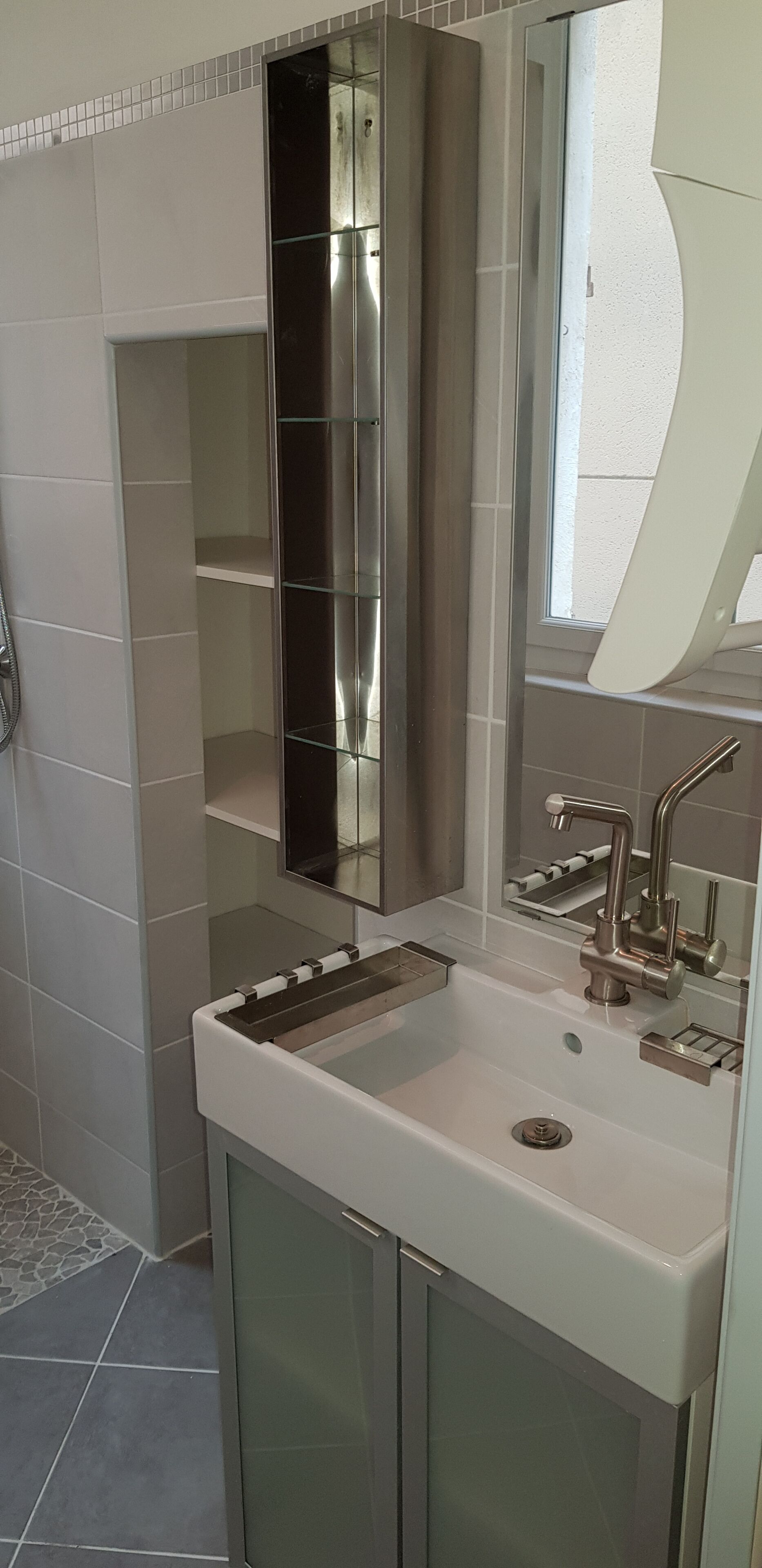 A bathroom with a white sink, stainless steel faucet, and a large mirror.