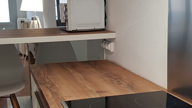 Una cocina moderna con encimera de madera, horno empotrado y microondas sobre un estante blanco.