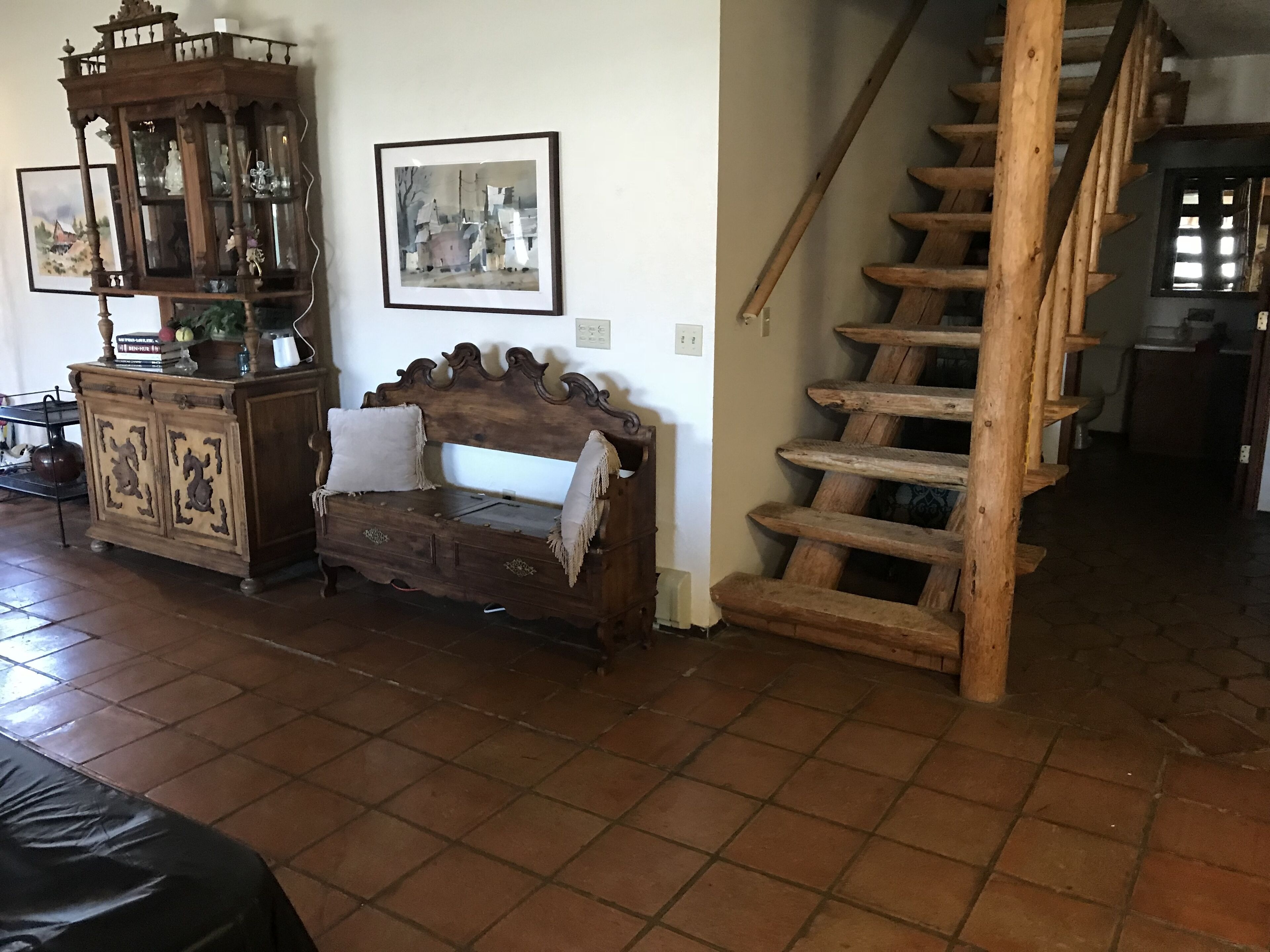 A wooden staircase with a rustic design, a wooden bench with decorative carvings, and a cabinet with glass doors.