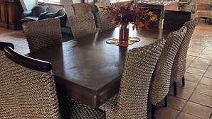 Un coin repas avec une grande table en bois entourée de chaises en osier, une cheminée en pierre et un buffet en bois doté de portes en verre.