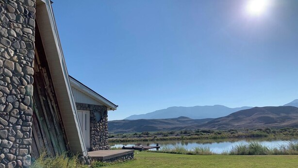 Un bâtiment en pierre doté d’une terrasse offrant une vue sur un lac et des montagnes.