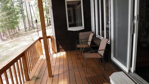 Eine Holzterrasse mit Glastür, einem kleinen Tisch und zwei Stühlen.