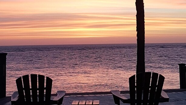 Two Adirondack chairs and a small table on a concrete surface by the ocean at sunset. - Relaxing beachfront condo (Fripp Island)
