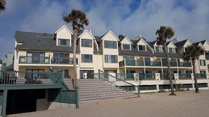 A beachfront hotel with multiple balconies, a staircase leading to the entrance, and palm trees. - Relaxing beachfront condo (Fripp Island)