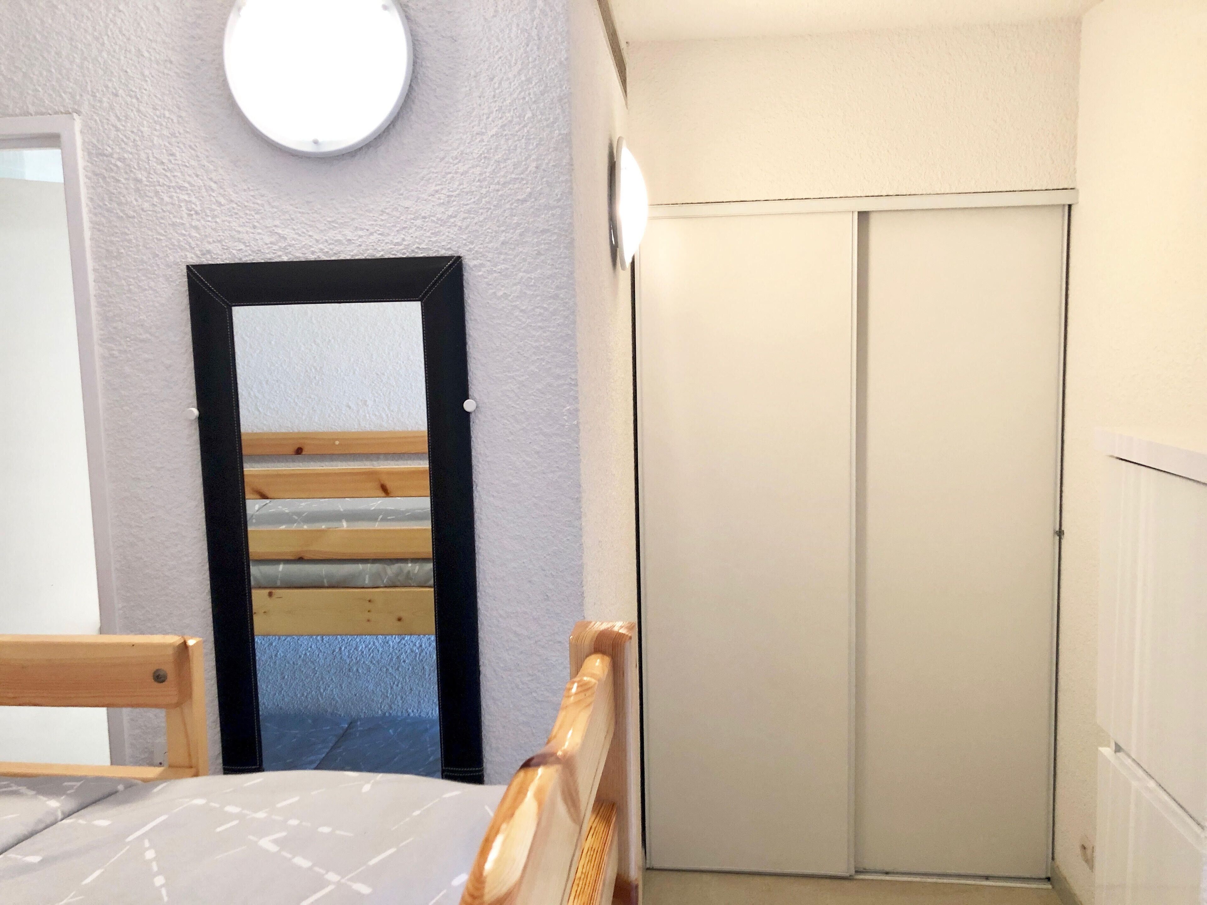 Quarto com cama, cabeceira de madeira, guarda-roupa e espelho na parede.
