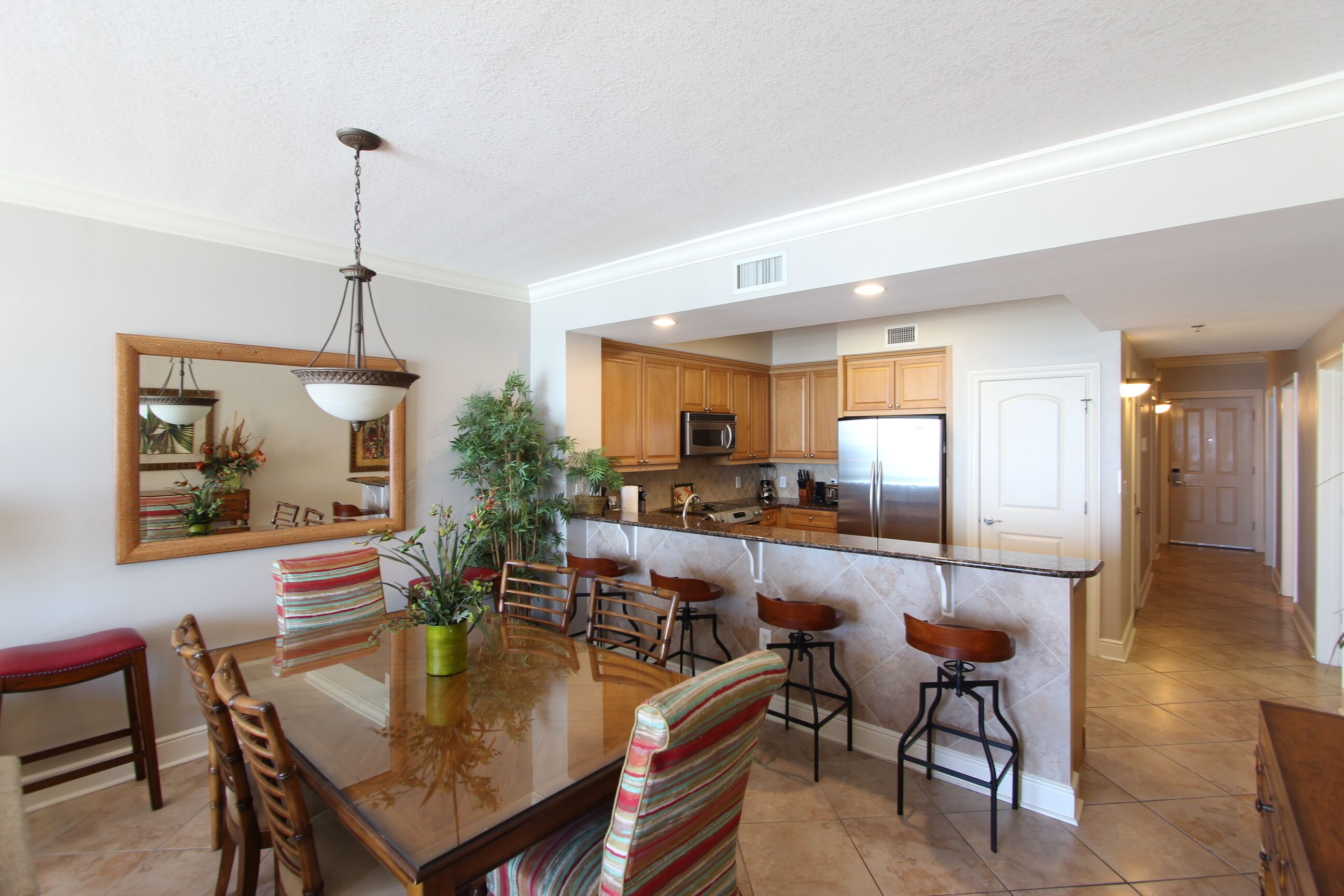 A modern kitchen with wooden cabinets, a stainless steel refrigerator, and a glass island with bar stools.