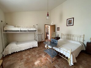 Ein Zimmer mit zwei Etagenbetten, einem kleinen Tisch mit Stuhl, einem Heizkörper und einer Tür zu einem weiteren Raum.