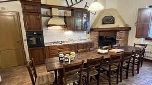 A kitchen with wooden cabinets, a dining table with chairs, a built-in oven, and a hanging light fixture. - Farmhouse Podere dell'Olmo in Umbria - Holiday Home (Ida's House) (Amelia)