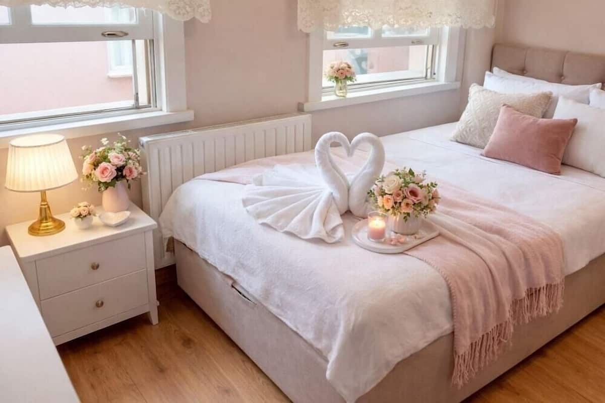 A bedroom with a bed, a nightstand, a lamp, a vase with flowers, and a window with lace curtains.