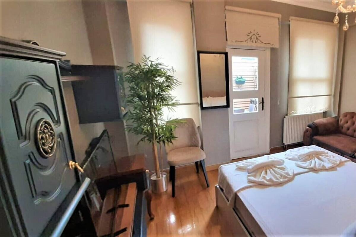 A bedroom with a bed, a sofa, a chair, a plant, a dresser, and a door with a window.