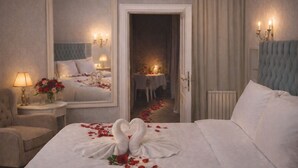 Habitación de hotel con una cama grande, una zona de estar con una silla y una mesa, un espejo y una puerta que da a un comedor.